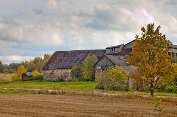 rural landscape, in the photo an old stone hayloft building and a wheat storage building against a gray sky with clouds