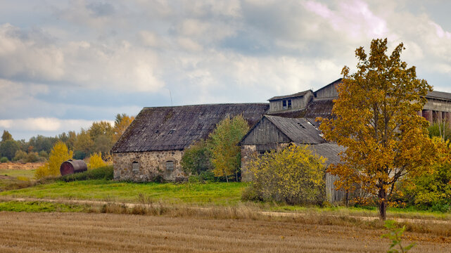 rural landscape, in the photo an old stone hayloft building and a wheat storage building against a gray sky with clouds