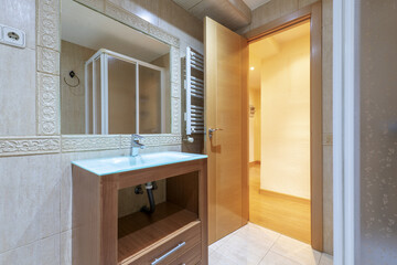 Small bathroom with tempered glass sink, wooden cabinet, white heated towel rail and mirror integrated into the wall, shower cabin and oak wood door