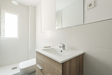 Small bathroom with white porcelain sink on wooden cabinet and frameless square mirror