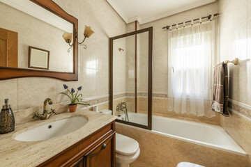 Bathroom with a white porcelain sink integrated into a cream-colored marble countertop on a vintage-style wooden cabinet and a mirror with a matching frame, a bathtub with a screen