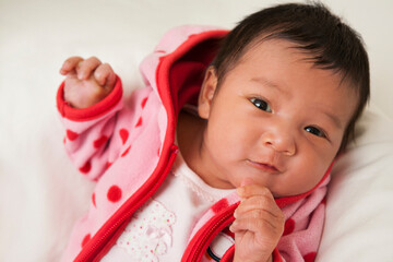 Close-up portrait of two week old Asian baby girl in pink polka dot jacket, smiling and looking at camera, studio shot