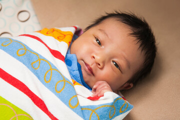 Close-up portrait of two week old, newborn Asian baby girl, wrapped in colorful swaddling blanket, studio shot