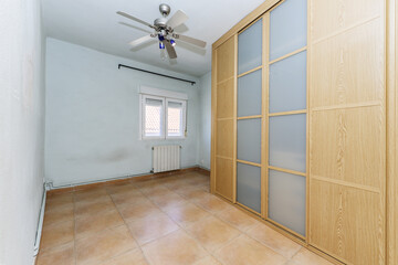 Empty room with a wall-to-wall built-in wardrobe with sliding doors made of oak wood and opaque...