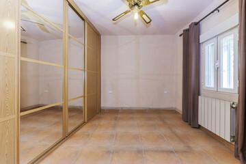 Empty room with wall to wall built-in wardrobe with oak sliding doors and mirrored ceiling fan,...