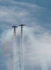 Obraz premium two light aircraft ascend in parallel leaving behind a white trail over the blue sky. condensation trails. concept together and beware