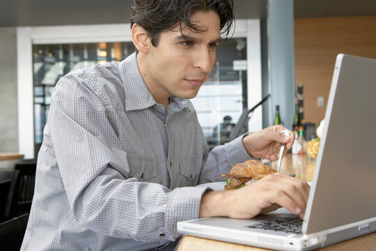 Man Using Laptop and Eating