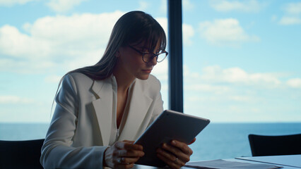 Office intern using tablet at panorama window. Focused woman analyzing data