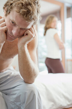 Man Sitting on Edge of Bed and Woman Standing by Window in Background