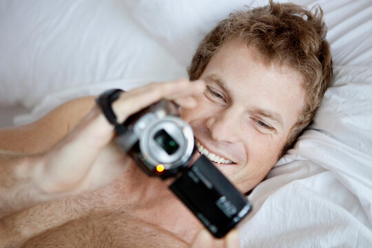 Man Lying in Bed Holding a Video Camera
