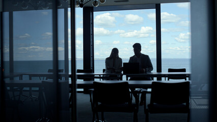 Business team silhouettes talking at sea clouds view. Two managers work laptop