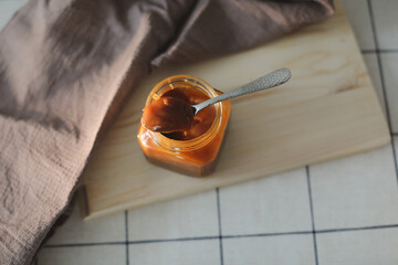Homemade salted caramel sauce in jar on rustic wooden table.