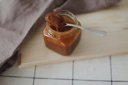Homemade salted caramel sauce in jar on rustic wooden table.