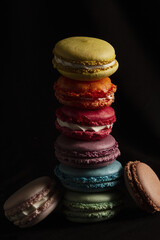 Colorful macarons stacked vertically on dark black background gourmet French pastry dessert, food photography