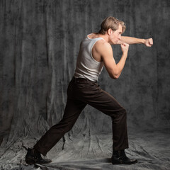 A sporty and athletic guy in a white T-shirt, boxing. A young man in a vintage outfit, posing in a studio on gray