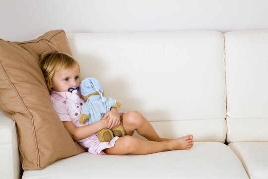Little Girl Sitting on Sofa, Holding Stuffed Animal