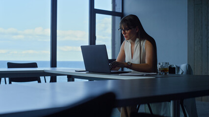 Office manager working computer at panorama window. Businesswoman looking laptop