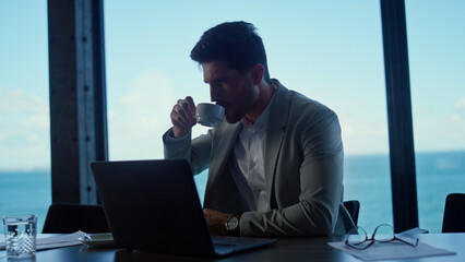 Serious business man looking computer in ocean view office. Boss using laptop