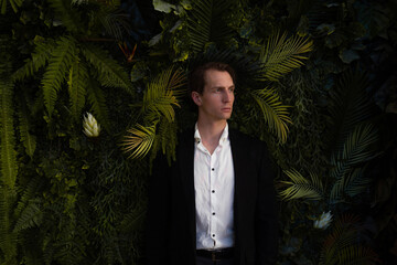 calm frontal portrait of a man in a business suit against a wall of plants, ferns and palm trees, a...