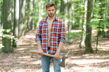 Naklejka na ściany i meble Unshaven man in lumberjack style standing with axe forest background