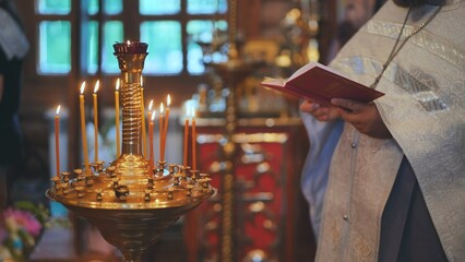 Burning candles against the background of the Priest reading the Bible at the service.