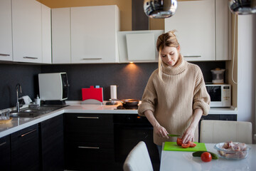 Lovely young woman at home in the kitchen, preparing a healthy meal. Beautiful charming blonde in her apartment