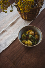 Bowl of roasted potatoes, mushrooms and greens on a white cloth with bright yellow tansy flowers