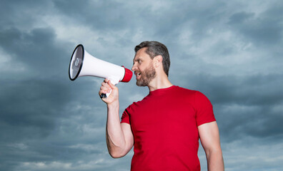 man in red shirt announcing in loudspeaker on sky background