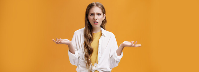 What, I do not understand. Portrait of arrogant questioned impolite girl being pissed with questiones shrugging with hands spread sideways making irritated grimace standing confused over orange wall - obrazy, fototapety, plakaty