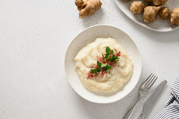 Jerusalem artichoke puree in plate decorated parsley on white background. View from above.