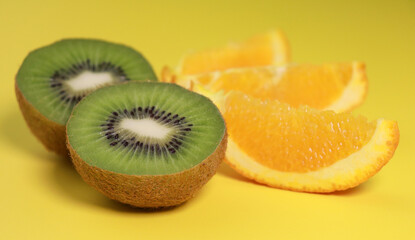 close up of kiwi fruit and orange slices on yellow background 