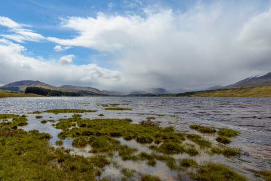 Grassy shoreline and dramatic cloud formations at Loch Tulla near Glen Coe in Scotland, United Kingdom