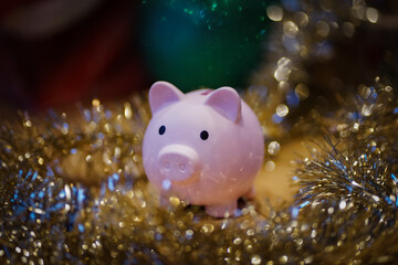close up of a pink piggy bank infront of a festively decorated christmas tree with balls and tinsel...