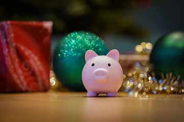 close up of a pink piggy bank infront of a festively decorated christmas tree with balls and tinsel...