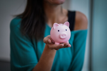 happy & sexy young woman with brown hair and pink piggy saving bank while smiling and looking up...