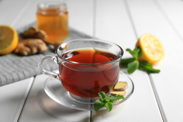 Cup of delicious ginger tea and ingredients on white wooden table, closeup