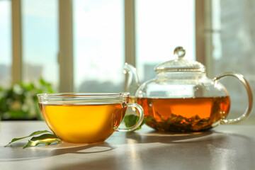 Fresh green tea in glass cup, leaves and teapot on table indoors