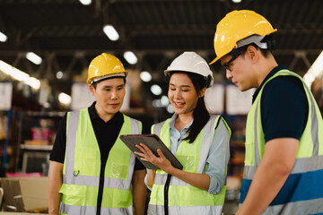 Asian Industrial Engineers talk with warehouse industrial workers using tablet to explain the procedure. They Work at the Heavy Industry Manufacturing Facility, industrial environment.