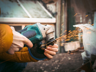 The hands of a young caucasian man in a yellow jacket are holding a drill and polishing with a disc