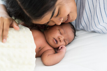 Top view mother kissing her newborn baby on bed. Young mom or nurse taking care newborn in the...