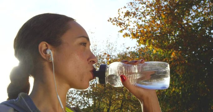 Music, fitness and woman drinking water before training in a park for health, sports and wellness with mockup. Radio, water and girl runner stop for break, hydration and relax during run in a forest