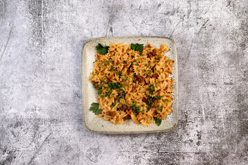 Farfalle pasta with beef stew on a square  plate on a dark background. Top view, flat lay
