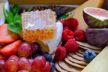 Close up front view of assortment of honey fruits cheeses crackers in a box. Concept for food delivery catering or gift for holiday season or packaging mock up. Selective focus