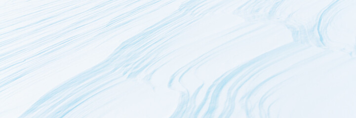 Wide panoramic winter background with snowy ground. Natural snow texture. Wind sculpted patterns on snow surface.