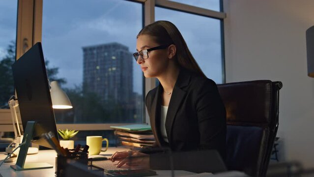 Beautiful manager typing computer in dark office. Pensive woman ponder business