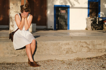 Girl in a summer light dress is crying on the street