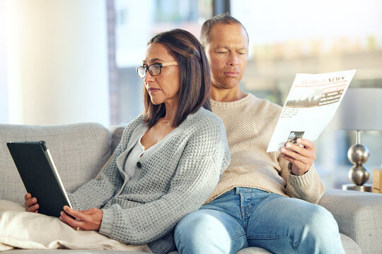 Tablet, Newspaper And Couple Relax On Sofa, Bonding And Streaming Video At Home. Technology, Love And Mature Man Reading News And Woman With Touchscreen On Social Media Or Internet Browsing In House.