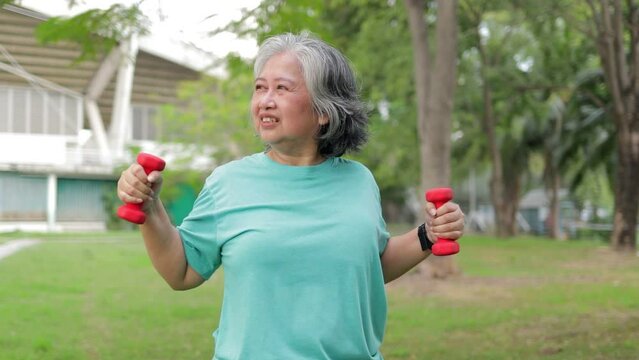 Asian senior woman exercising outdoors Hold dumbbells to build arm muscles. Sport concept, healthy exercise. lose weight