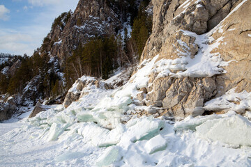 Fototapeta na wymiar Winter landscape, mountains and rocks covered with forest, on the bank of a frozen river.