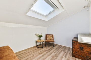a room with wood floors and skylights on the roof, including a brown chair in front of a white wall